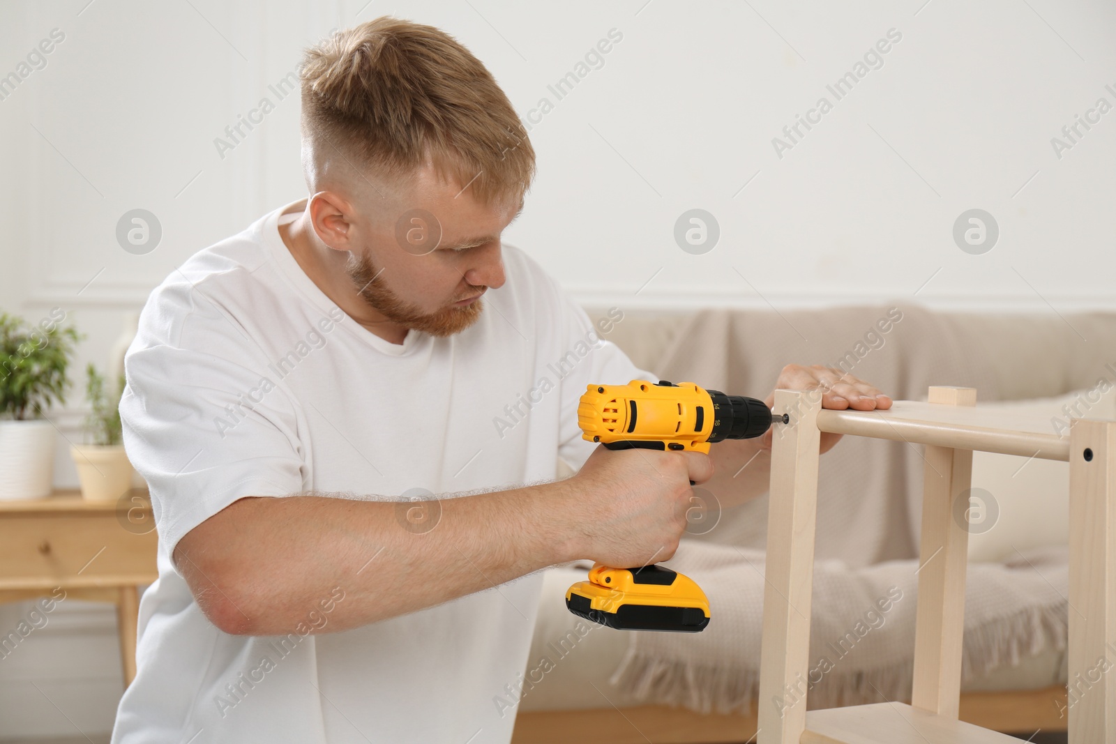 Photo of Man with electric screwdriver assembling furniture in room