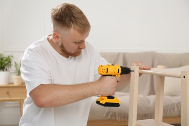 Photo of Man with electric screwdriver assembling furniture in room