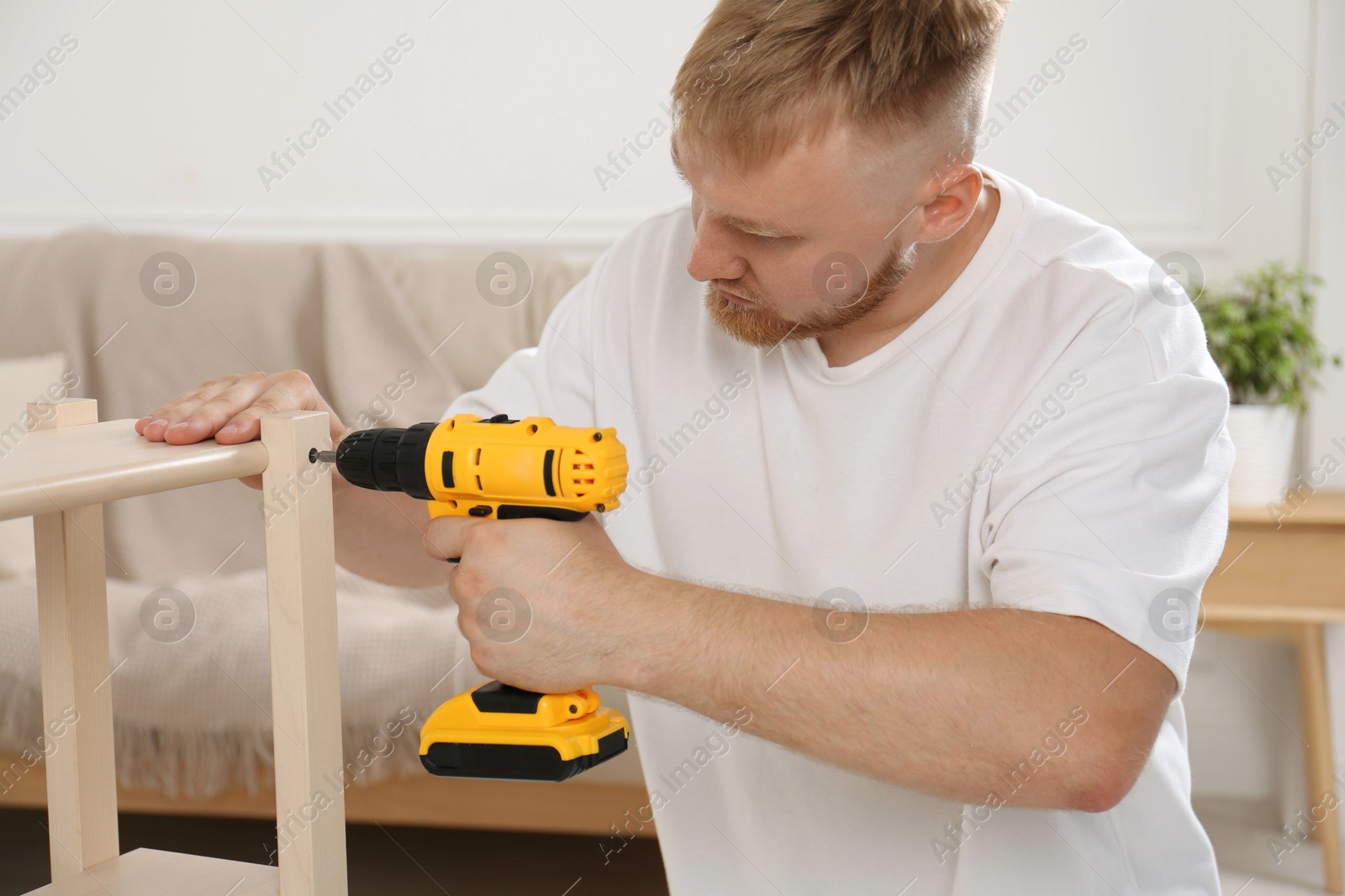 Photo of Man with electric screwdriver assembling furniture in room