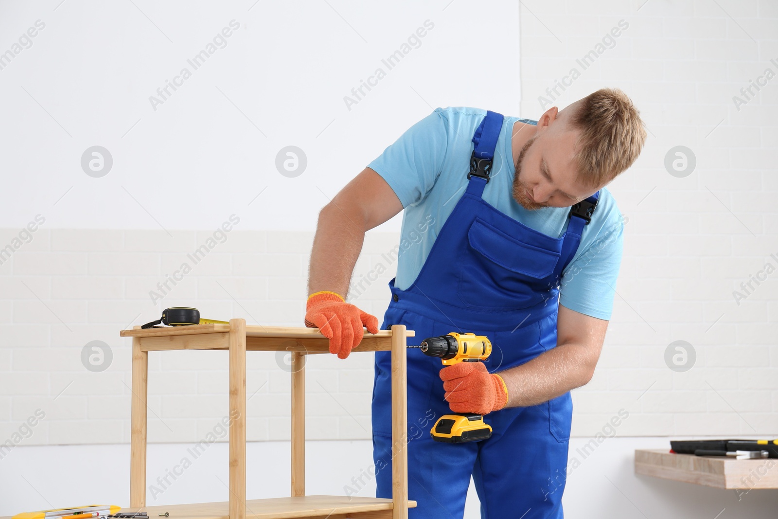 Photo of Worker with electric screwdriver assembling furniture indoors