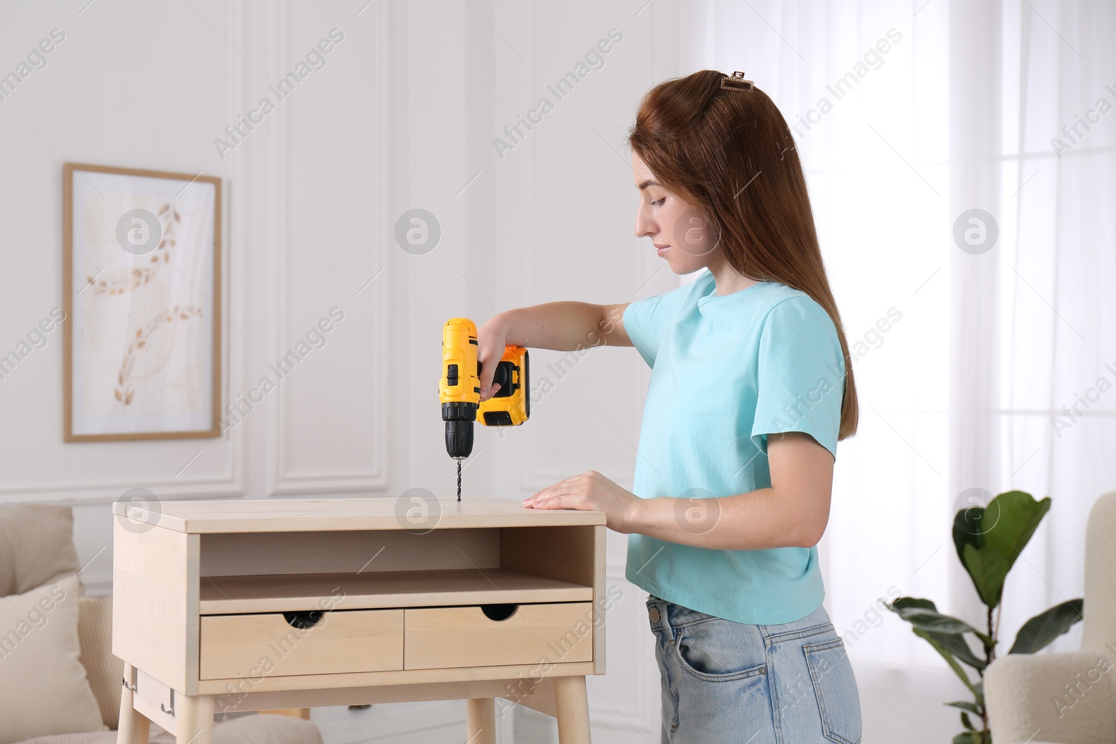 Photo of Woman with electric screwdriver assembling table in room