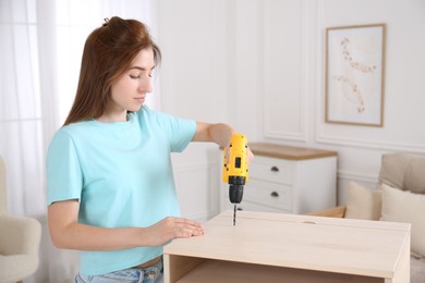 Woman with electric screwdriver assembling table in room