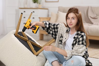 Photo of Woman with electric screwdriver assembling armchair at home