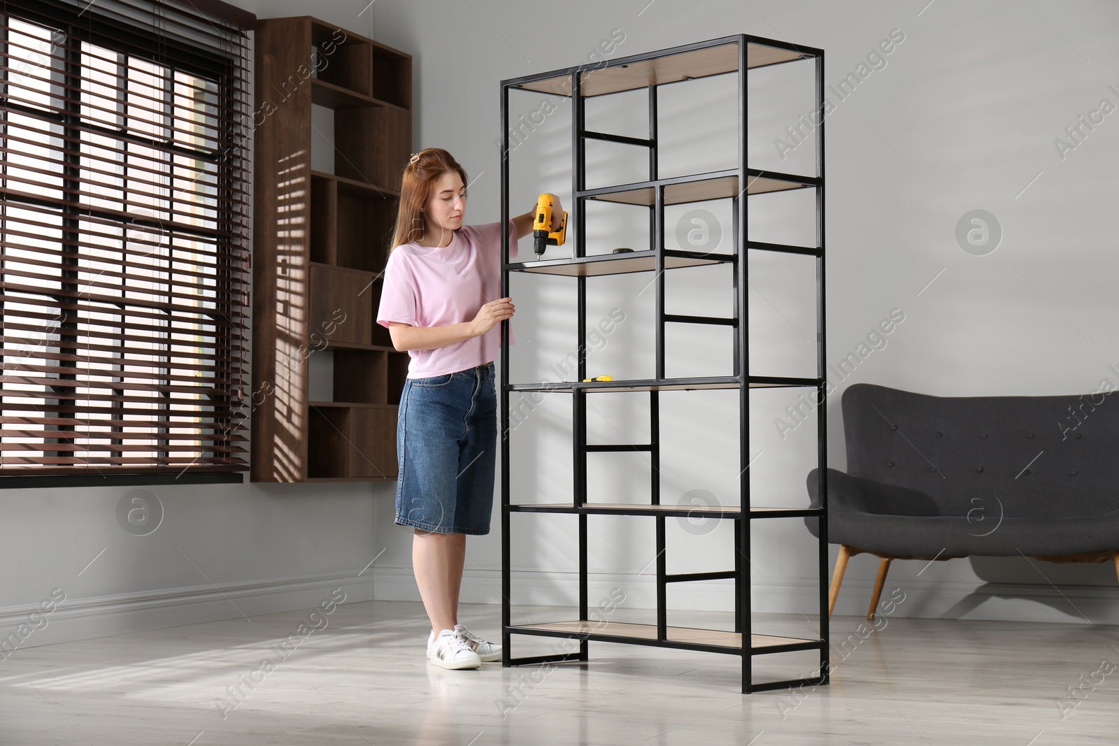 Photo of Woman with electric screwdriver assembling shelving unit in room