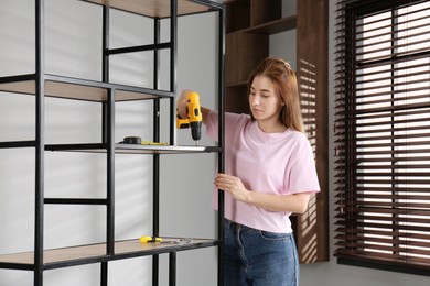 Woman with electric screwdriver assembling shelving unit in room