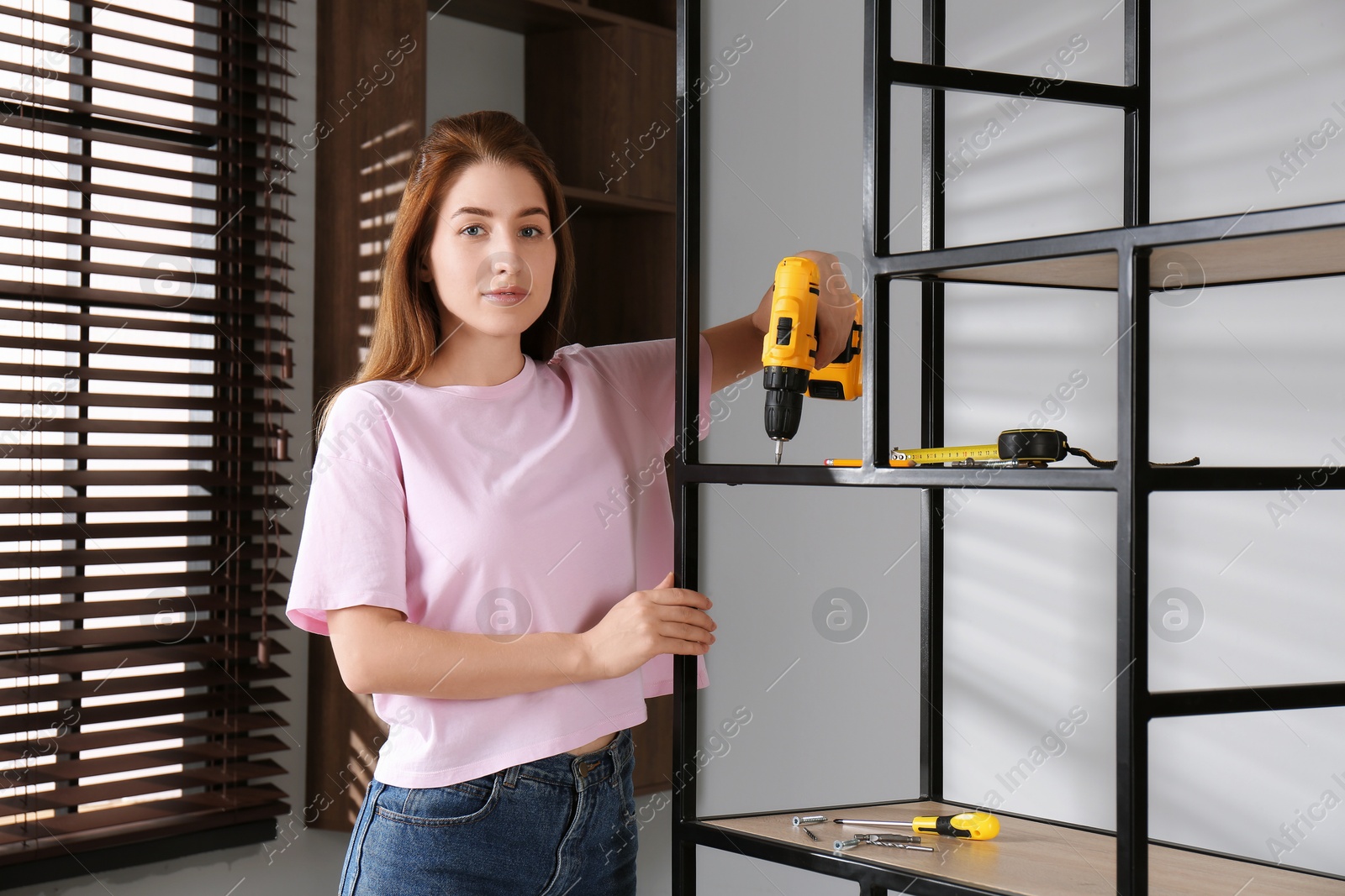 Photo of Woman with electric screwdriver assembling shelving unit in room