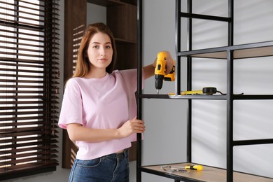 Woman with electric screwdriver assembling shelving unit in room