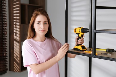 Woman with electric screwdriver assembling shelving unit in room