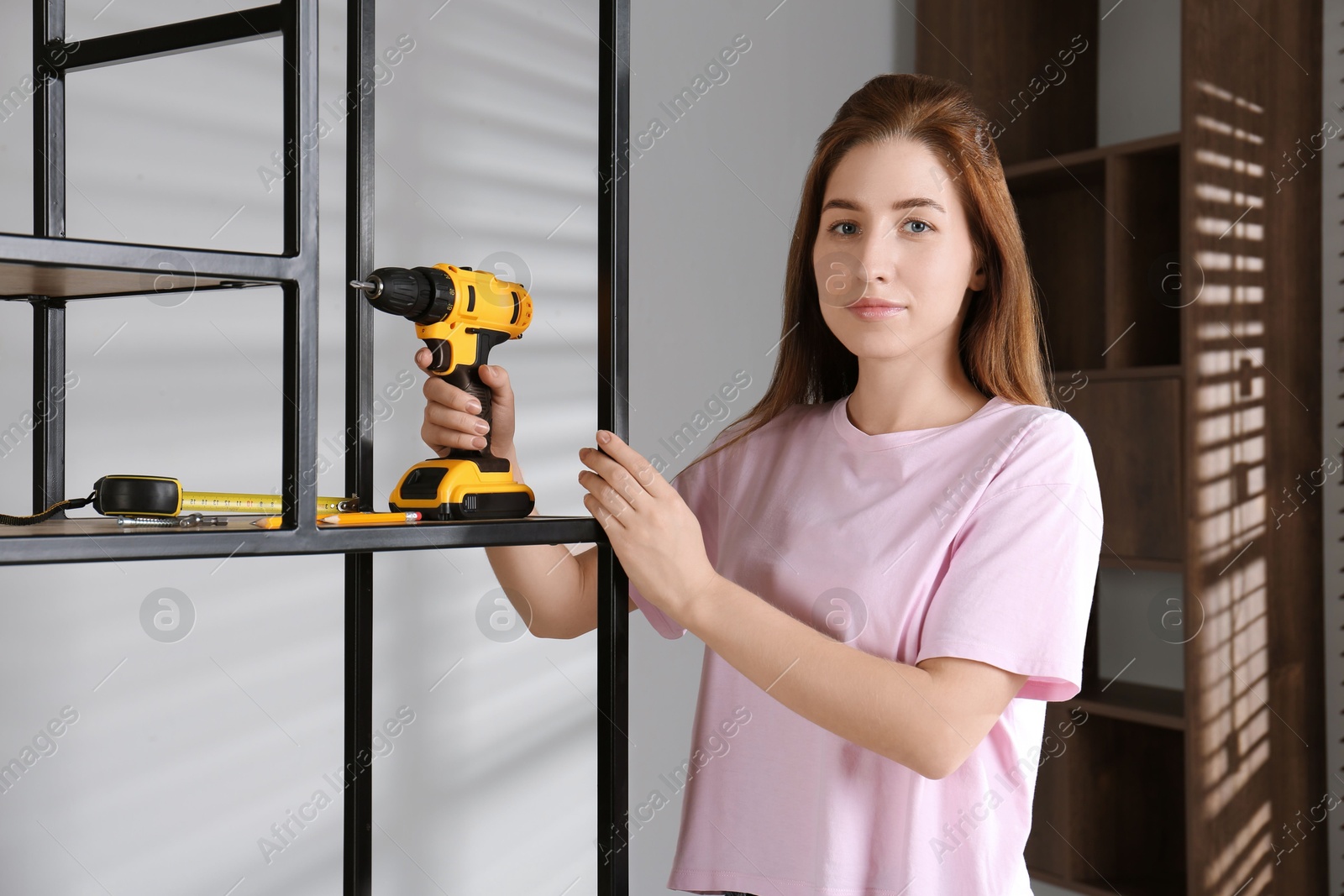 Photo of Woman with electric screwdriver assembling shelving unit in room