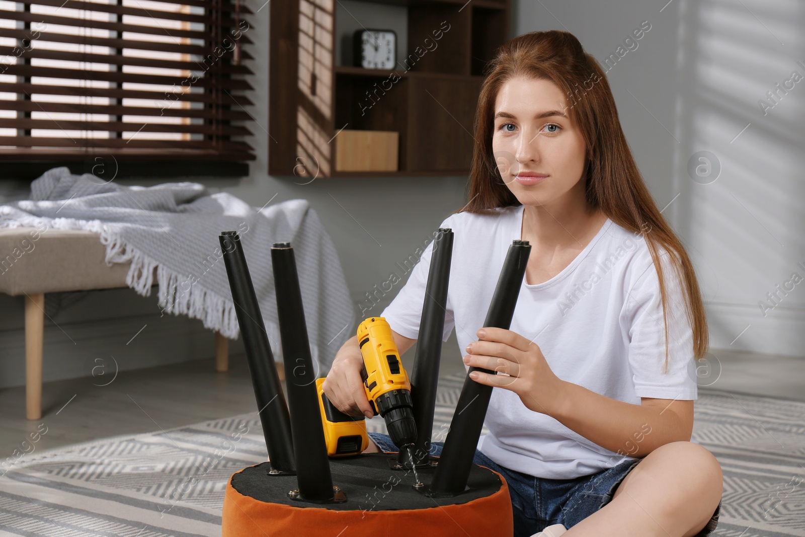 Photo of Woman with electric screwdriver assembling pouf at home