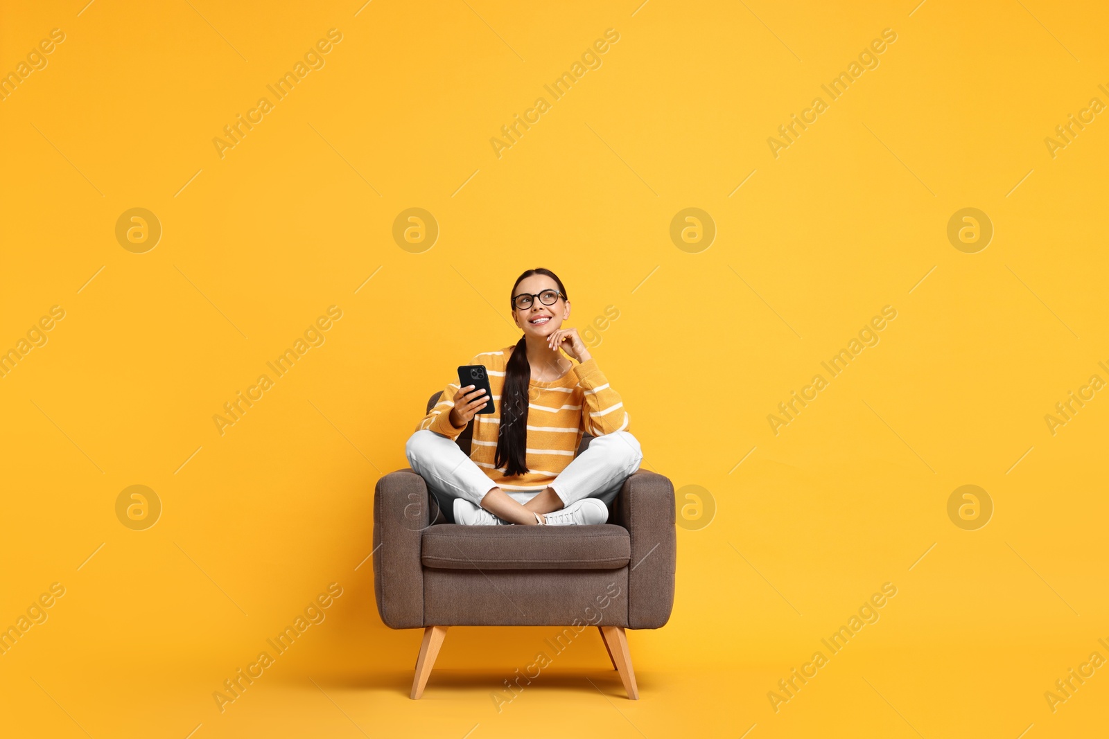 Photo of Smiling woman with smartphone sitting on armchair against yellow background