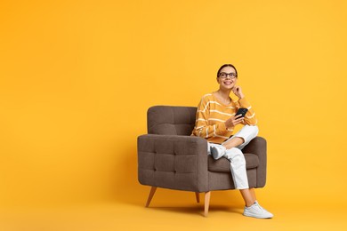 Photo of Smiling woman with smartphone sitting on armchair against yellow background. Space for text