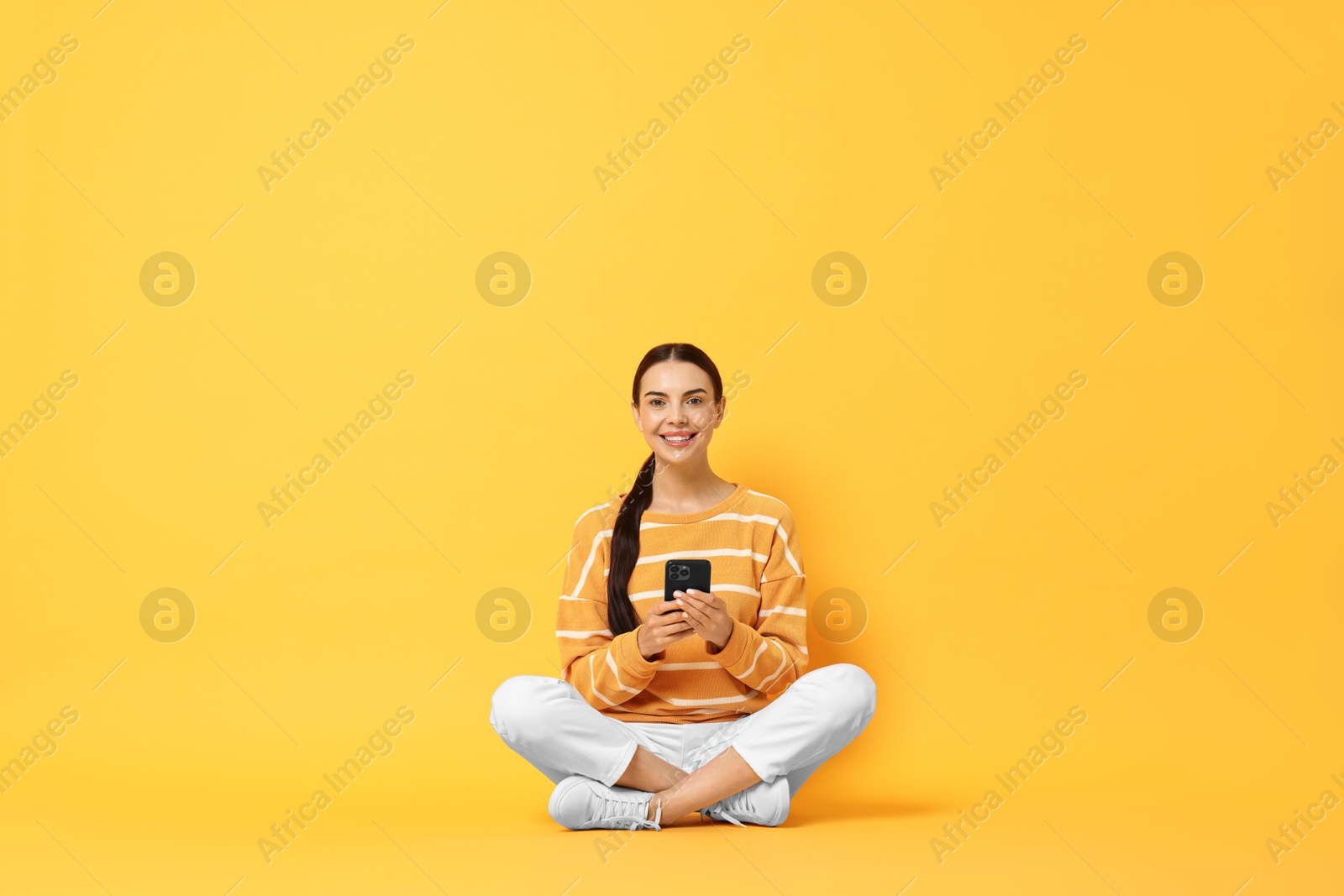 Photo of Happy woman with smartphone on yellow background