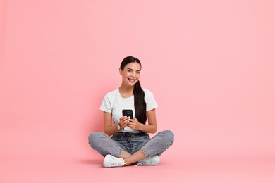 Photo of Smiling woman with smartphone on pink background