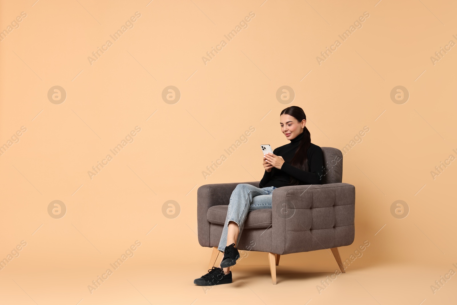 Photo of Beautiful woman with smartphone sitting on armchair against beige background. Space for text