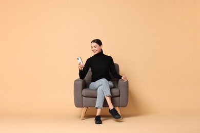 Photo of Smiling woman with smartphone sitting on armchair against beige background