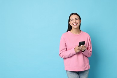 Photo of Smiling woman with smartphone on light blue background. Space for text