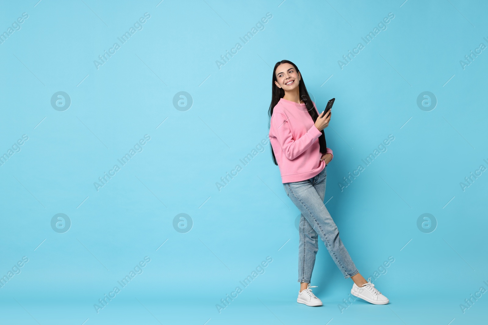 Photo of Smiling woman with smartphone on light blue background. Space for text