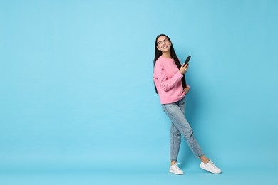 Photo of Smiling woman with smartphone on light blue background. Space for text