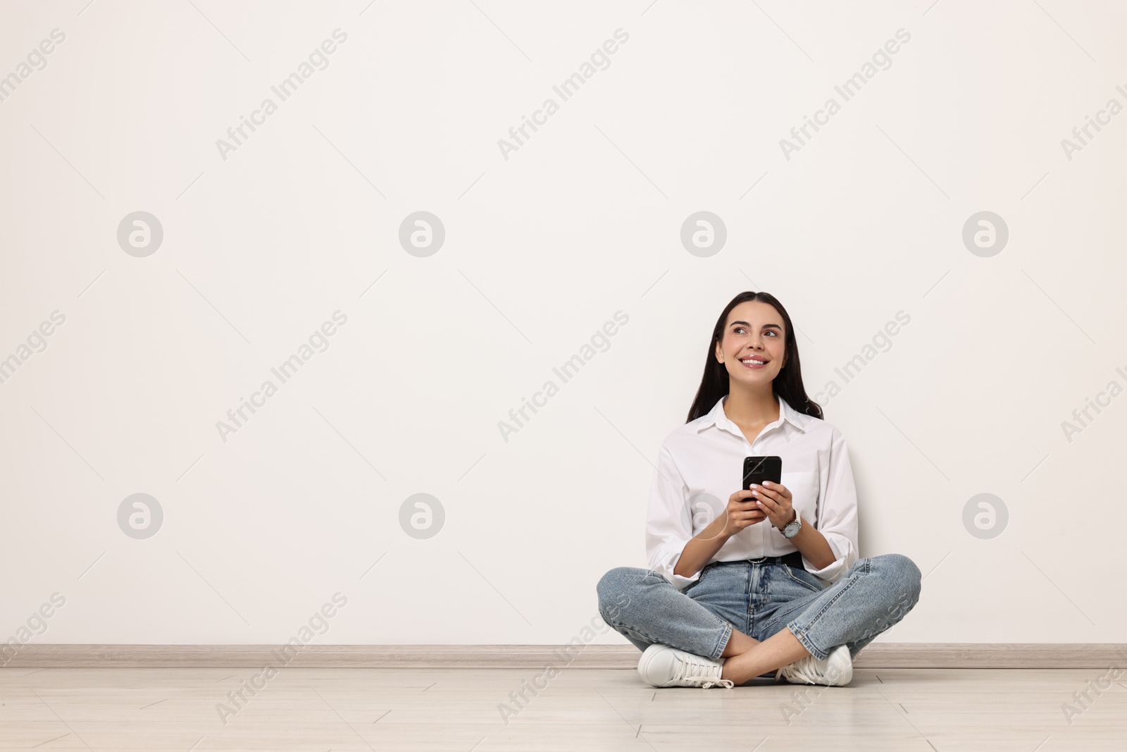 Photo of Smiling woman with smartphone on floor against white background. Space for text