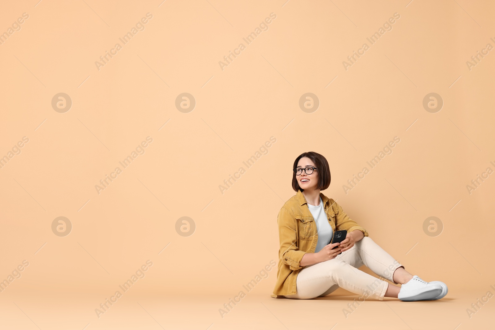 Photo of Smiling woman with smartphone sitting on beige background. Space for text