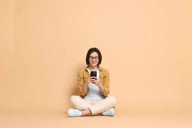 Photo of Smiling woman with smartphone sitting on beige background