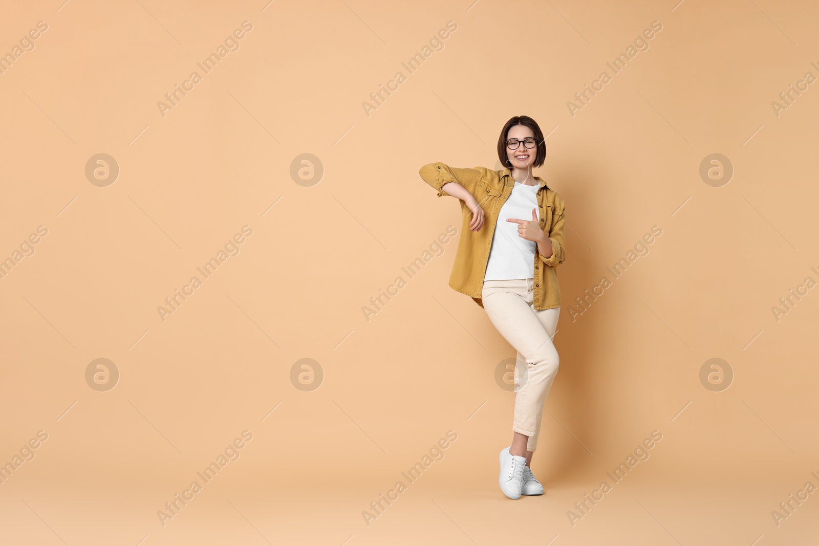 Photo of Smiling woman pointing at something on beige background. Space for text