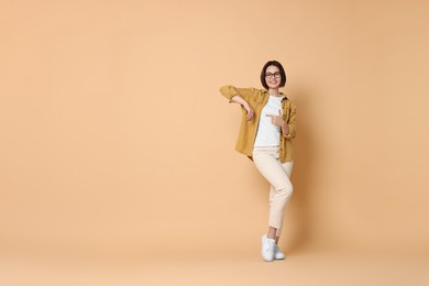 Smiling woman pointing at something on beige background. Space for text