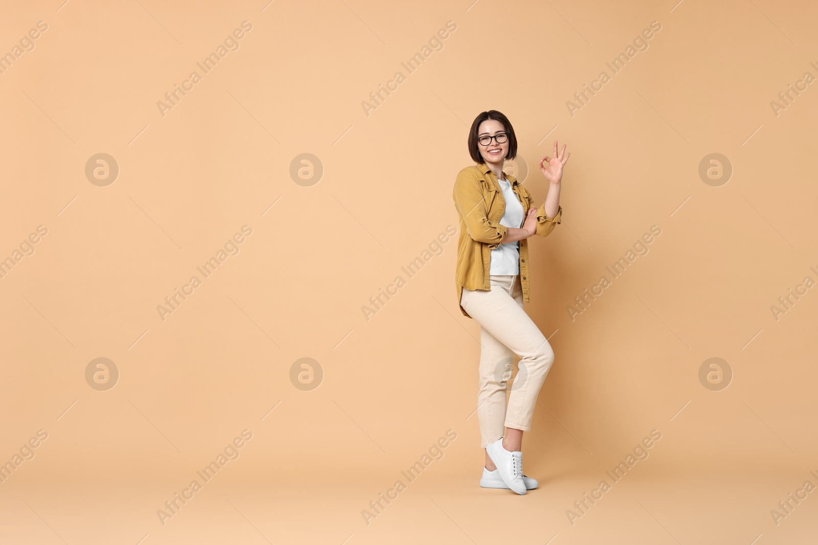 Photo of Smiling woman showing ok gesture on beige background. Space for text