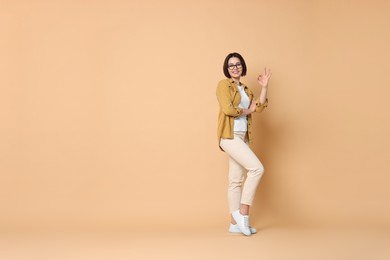 Photo of Smiling woman showing ok gesture on beige background. Space for text