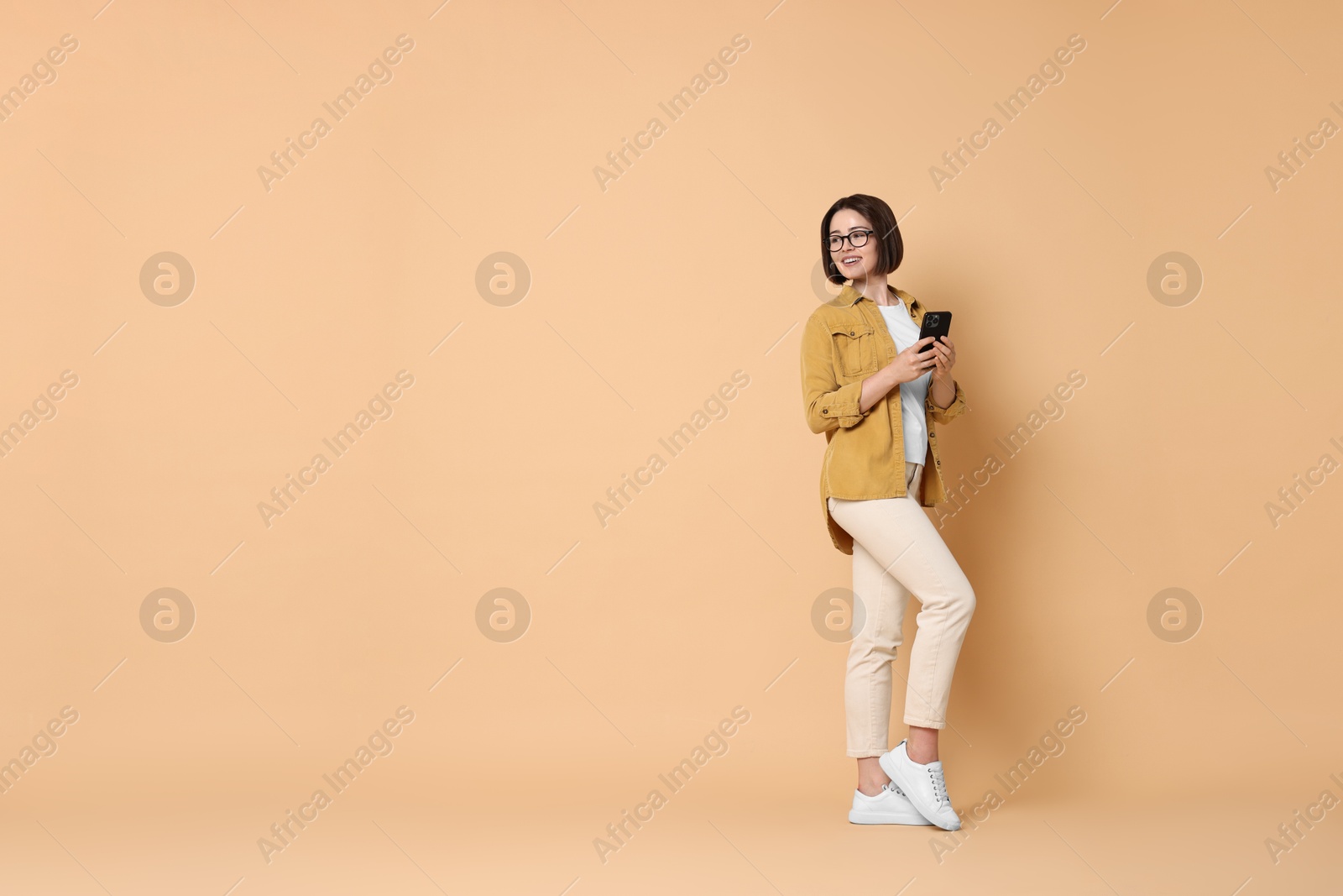 Photo of Smiling woman with smartphone on beige background. Space for text