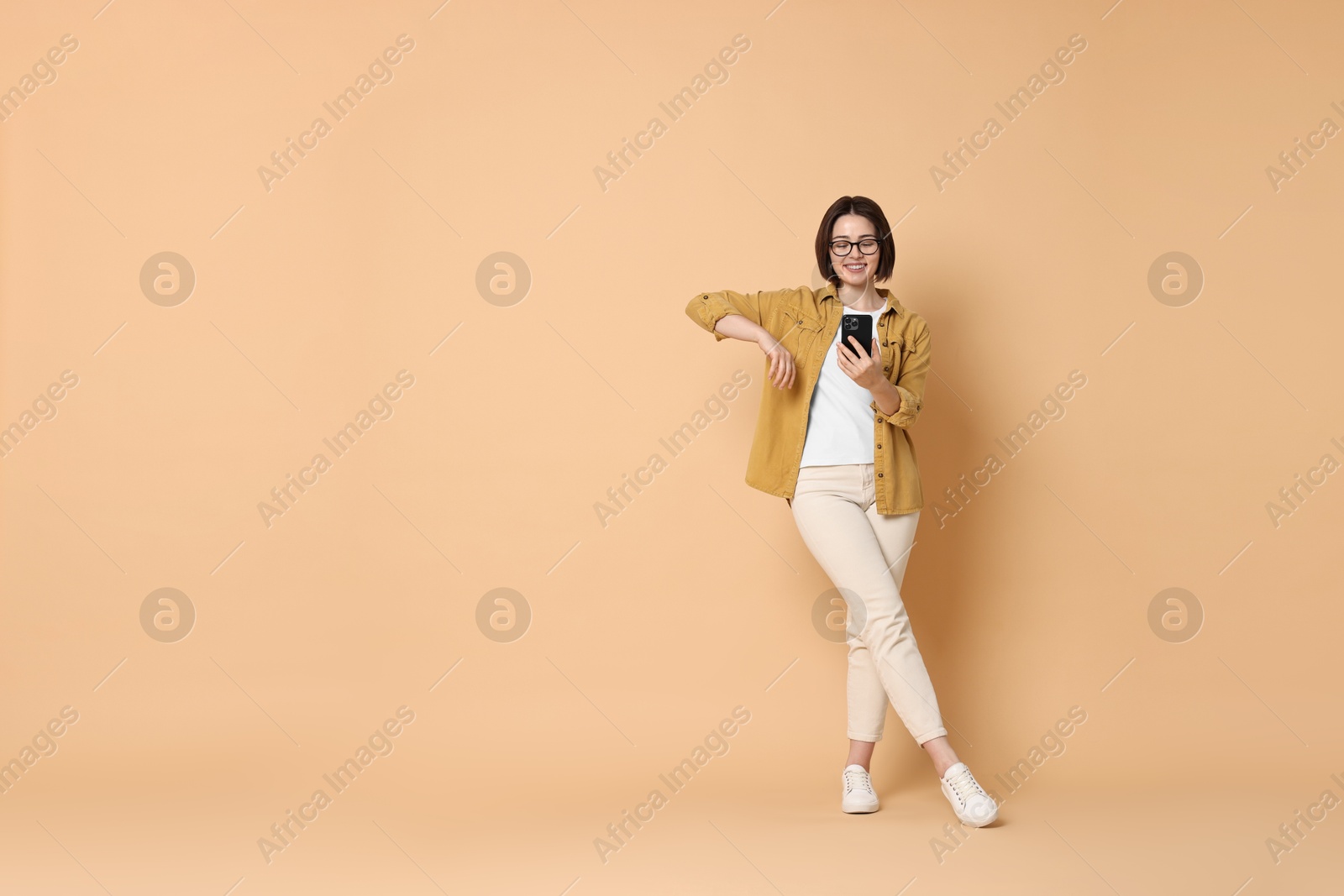 Photo of Smiling woman with smartphone on beige background. Space for text