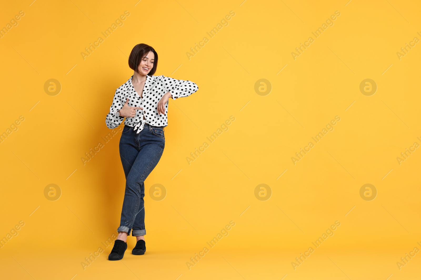 Photo of Smiling woman pointing at something on yellow background. Space for text