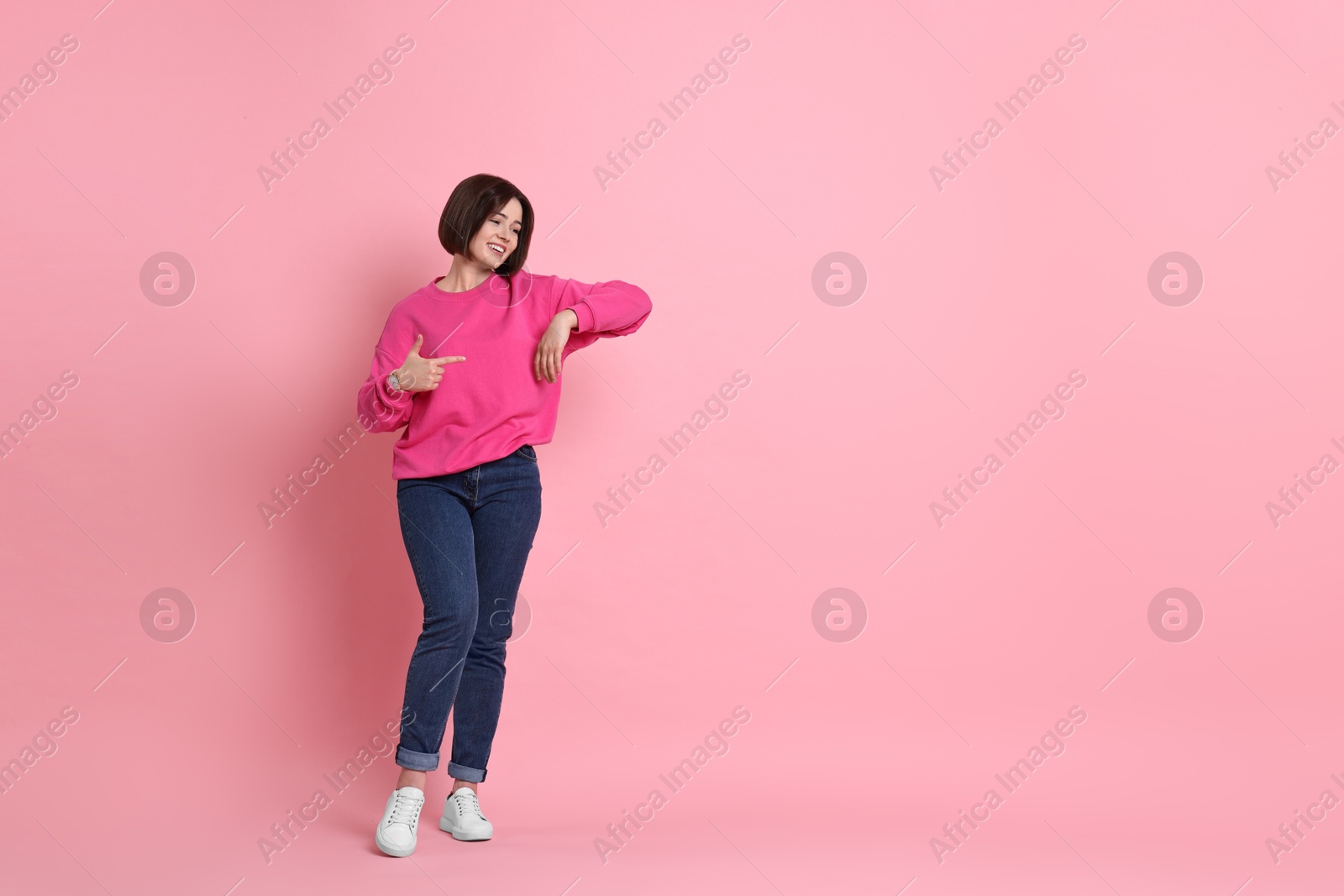 Photo of Smiling woman pointing at something on pink background. Space for text