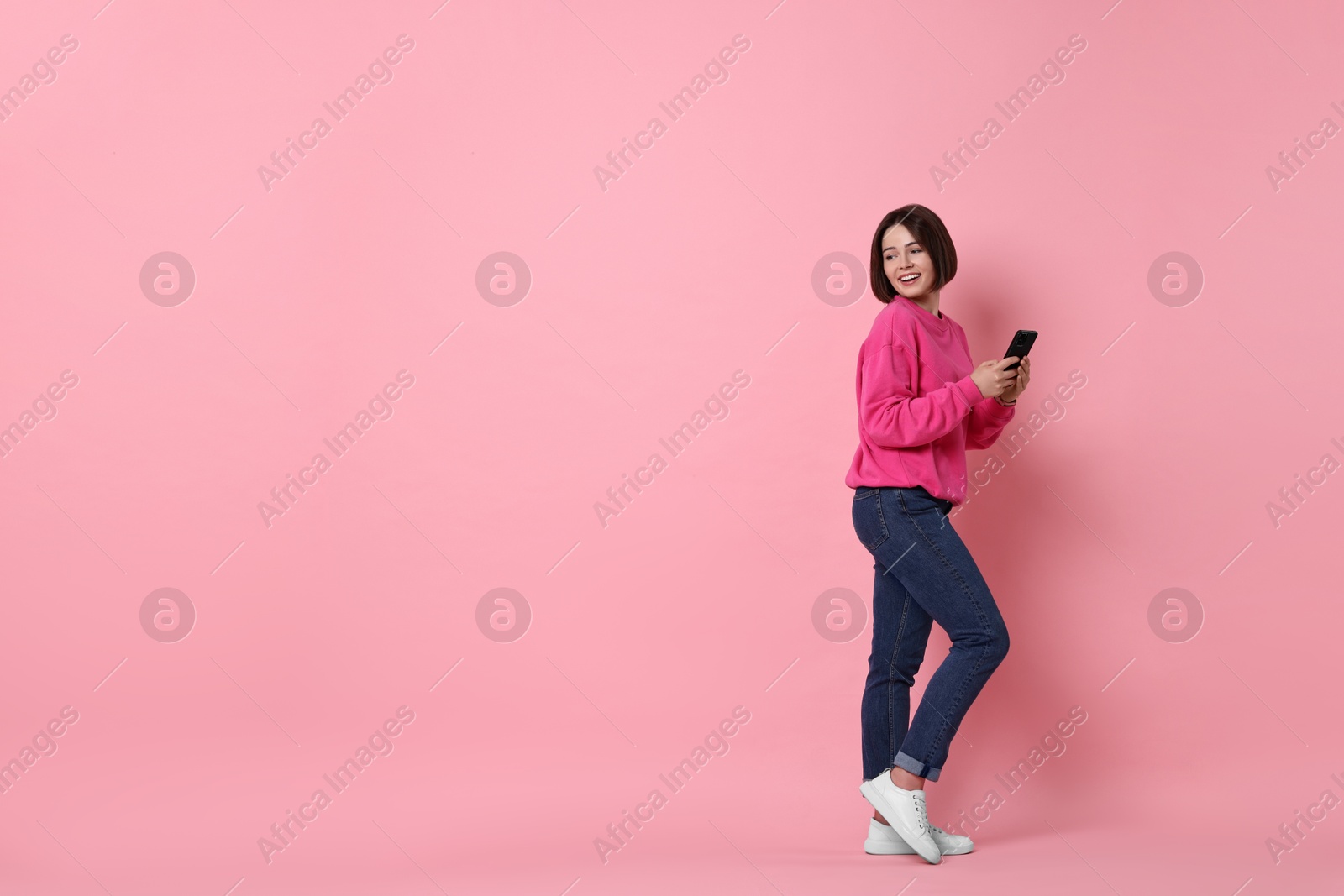 Photo of Smiling woman with smartphone on pink background. Space for text