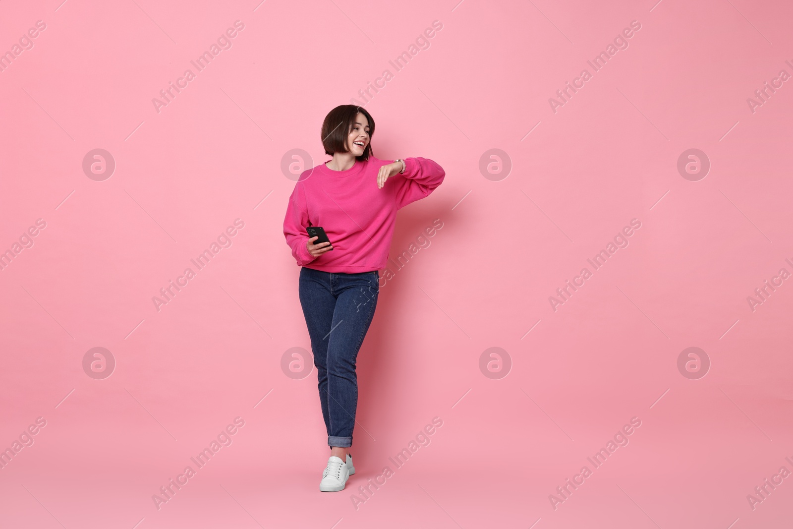 Photo of Smiling woman with smartphone on pink background. Space for text