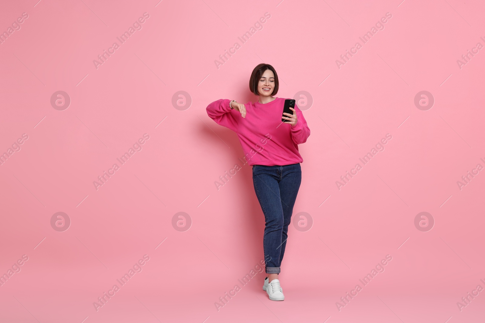 Photo of Smiling woman with smartphone on pink background. Space for text