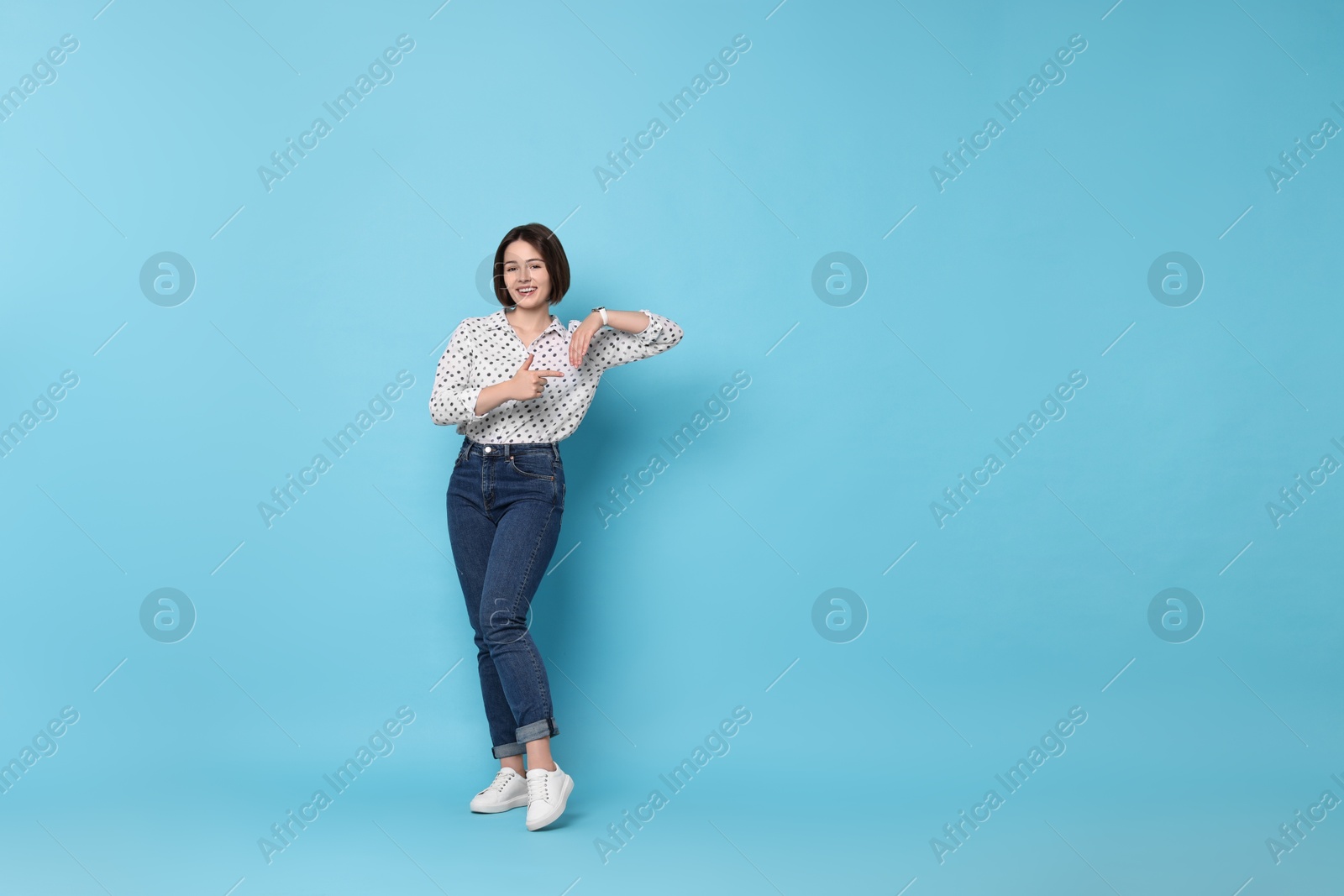 Photo of Happy woman pointing at something on light blue background. Space for text