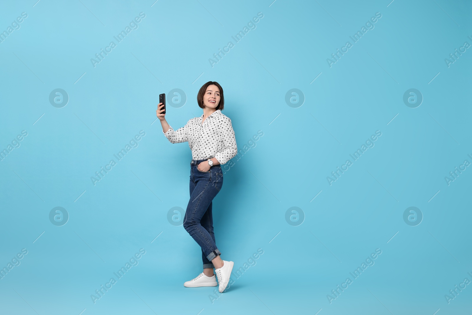 Photo of Smiling woman with smartphone on light blue background. Space for text