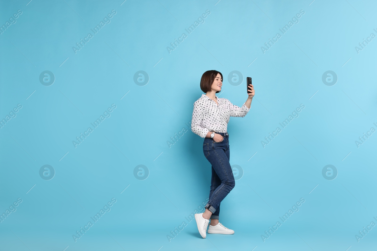 Photo of Smiling woman with smartphone on light blue background. Space for text