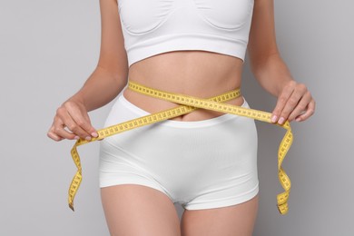 Diet and weight loss concept. Woman with measuring tape showing her slim body against light grey background, closeup