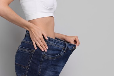 Photo of Diet and weight loss concept. Woman in big jeans showing her slim body on white background, closeup. Space for text