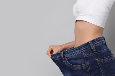 Photo of Diet and weight loss concept. Woman in big jeans showing her slim body on white background, closeup. Space for text