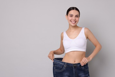 Photo of Diet and weight loss concept. Happy young woman in big jeans showing her slim body on light grey background. Space for text