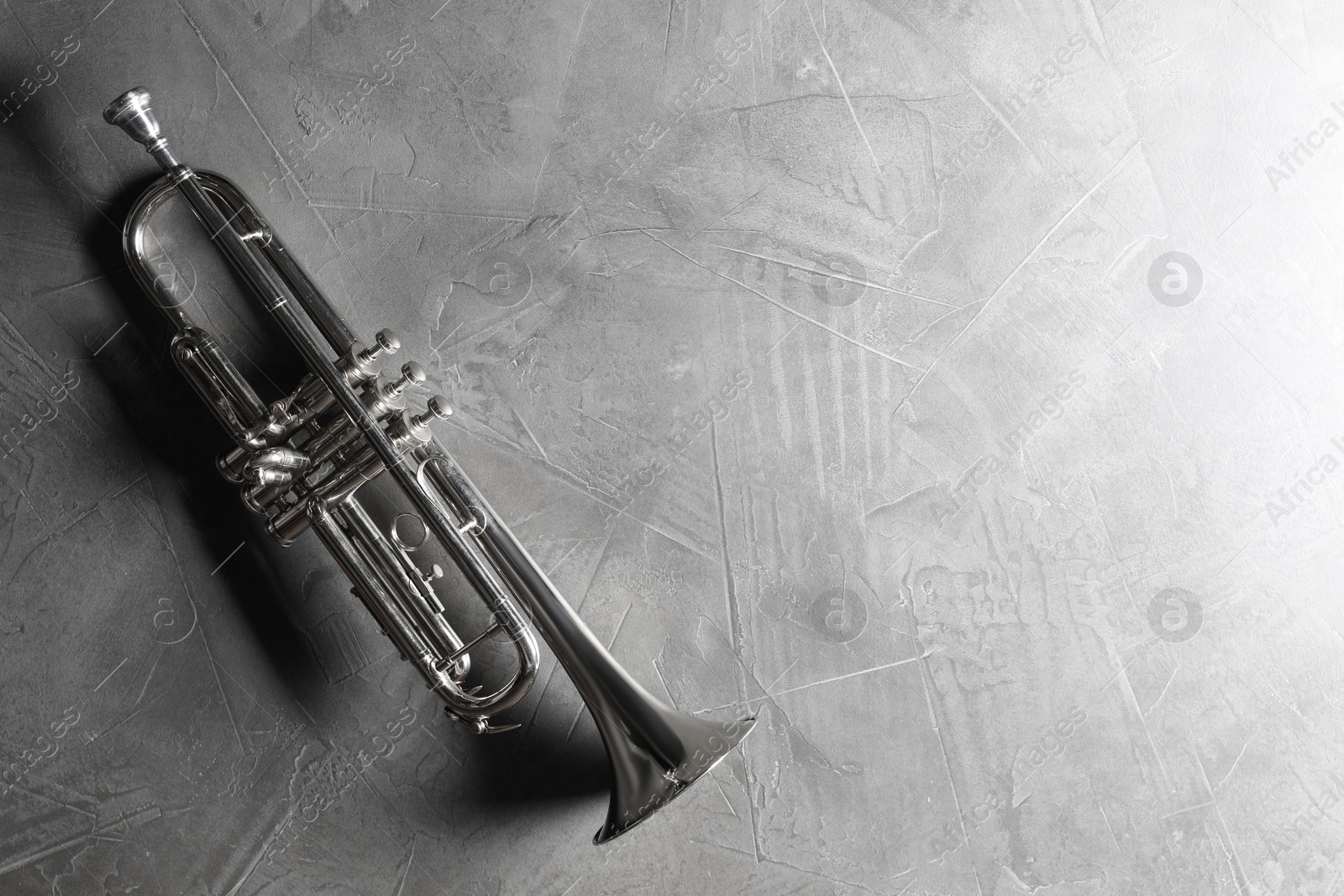 Photo of Shiny trumpet on grey textured table, top view. Space for text. Wind musical instrument