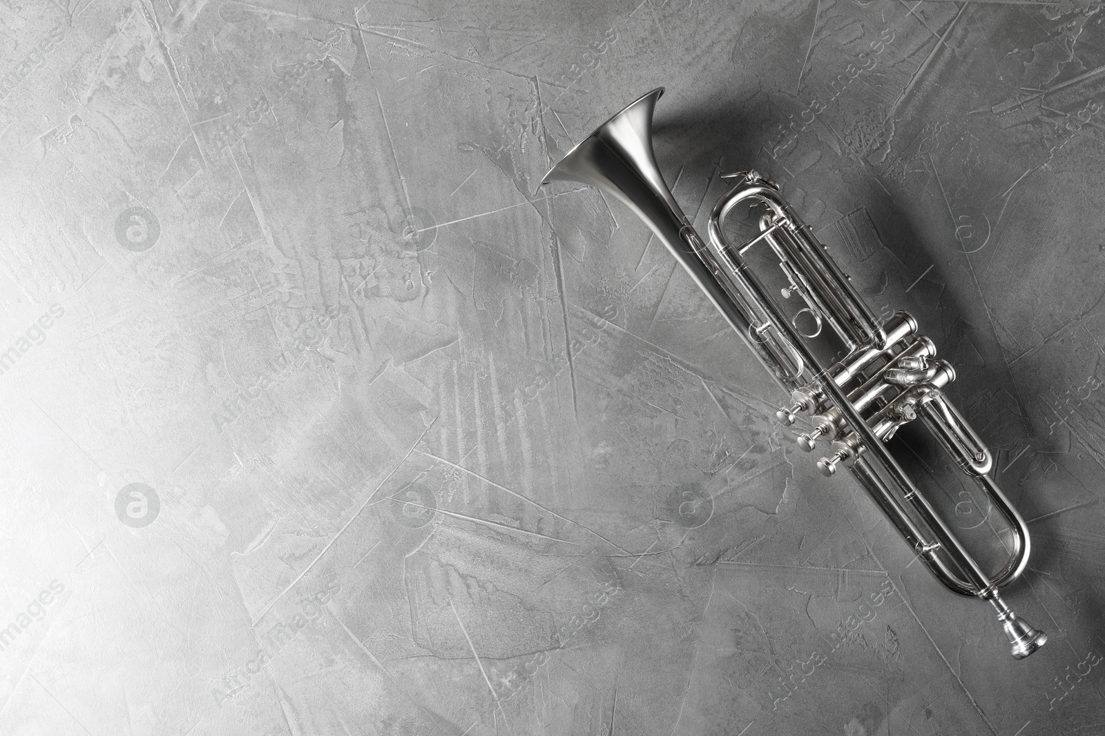 Photo of Shiny trumpet on grey textured table, top view. Space for text. Wind musical instrument