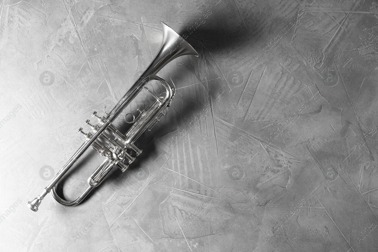 Photo of Shiny trumpet on grey textured table, top view. Space for text. Wind musical instrument