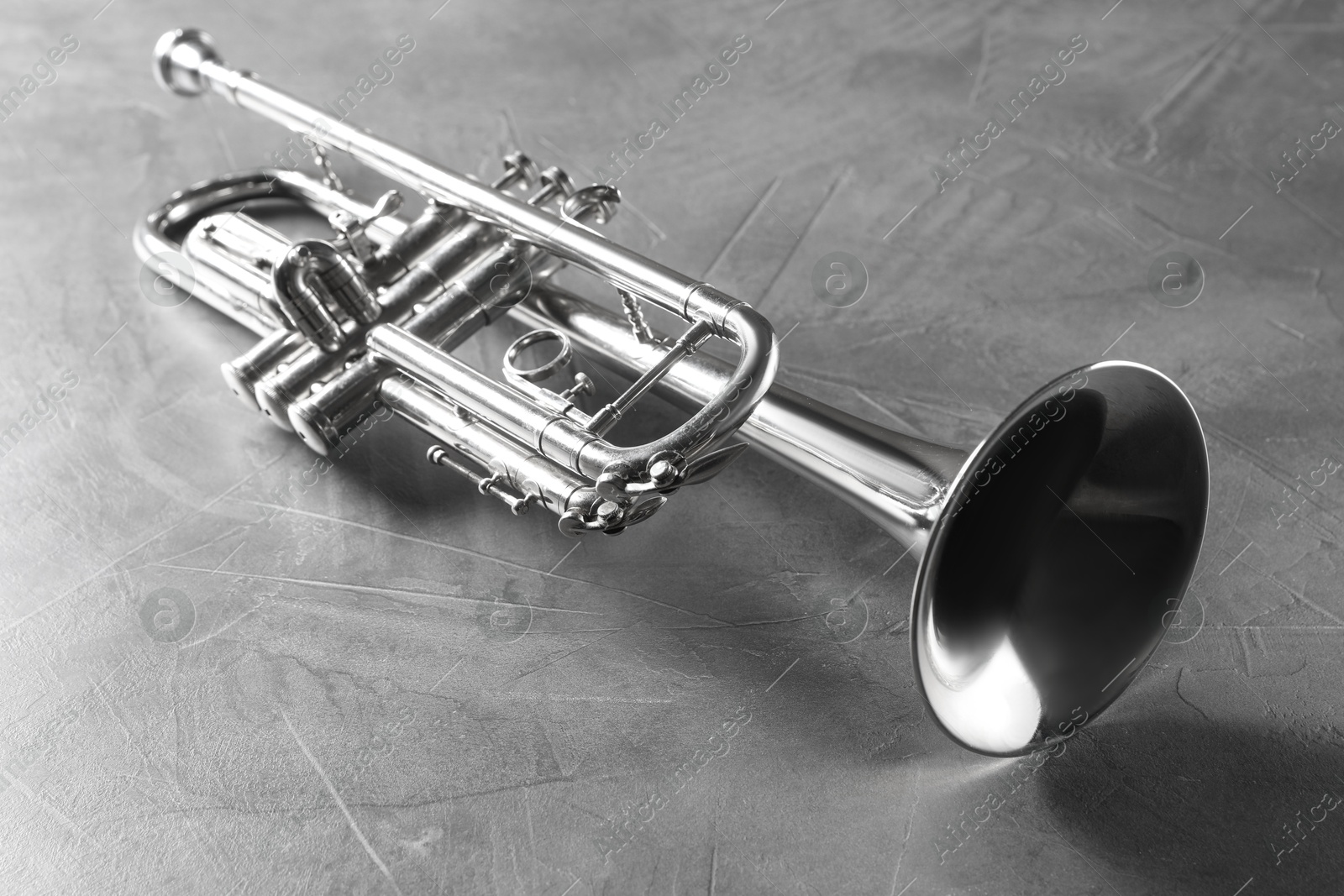 Photo of Shiny trumpet on grey textured table. Wind musical instrument