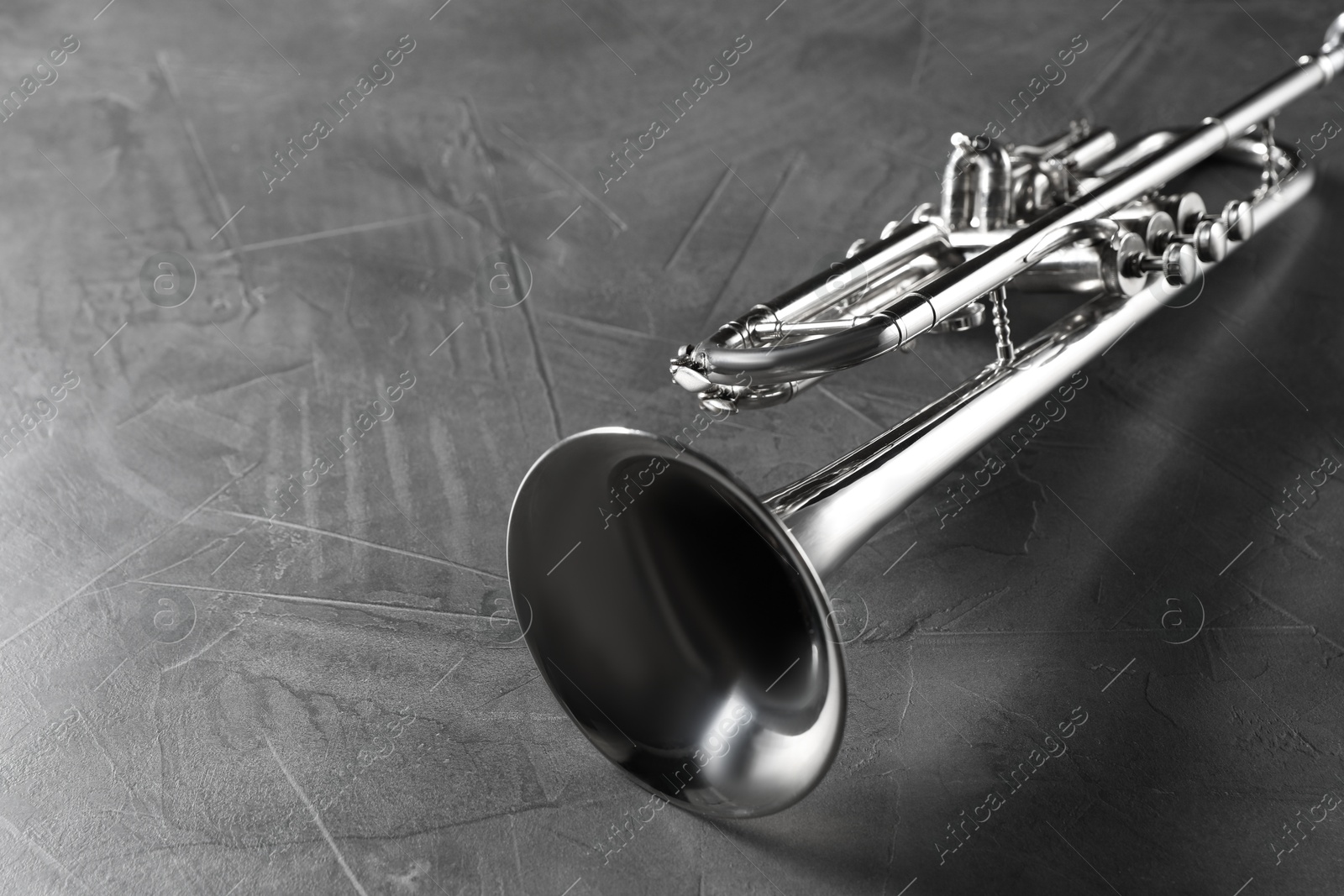 Photo of Closeup view of shiny trumpet on grey textured table. Wind musical instrument