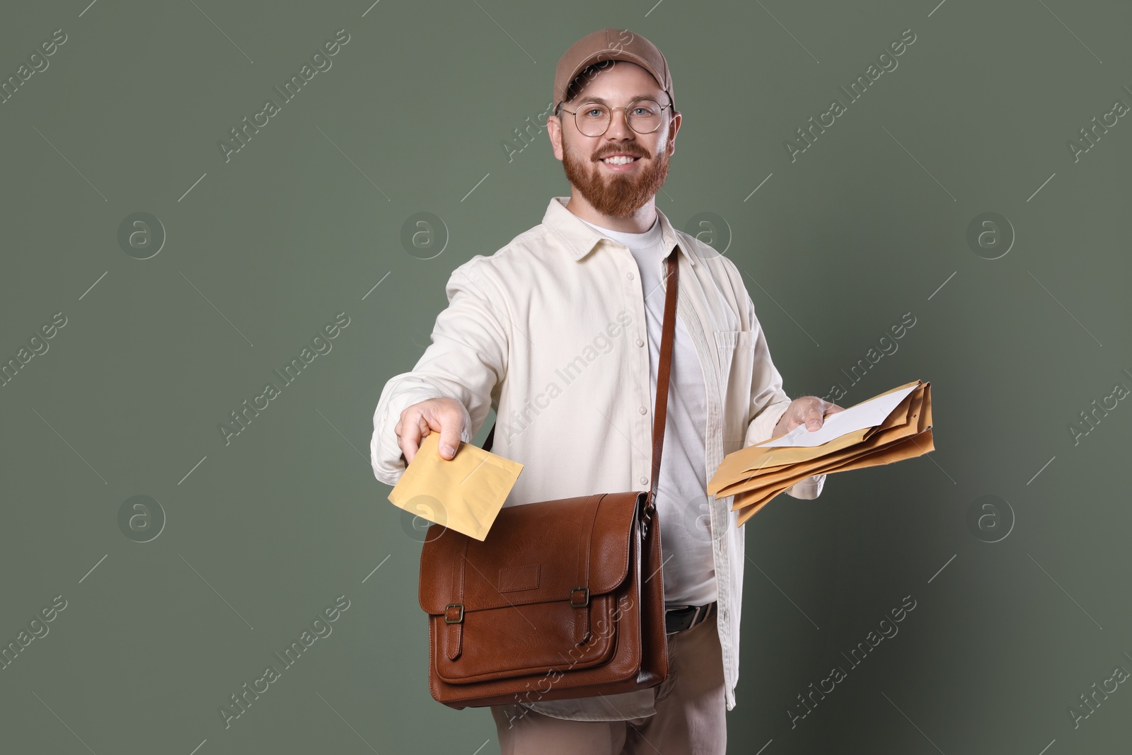 Photo of Happy young postman with brown bag delivering letters on olive background